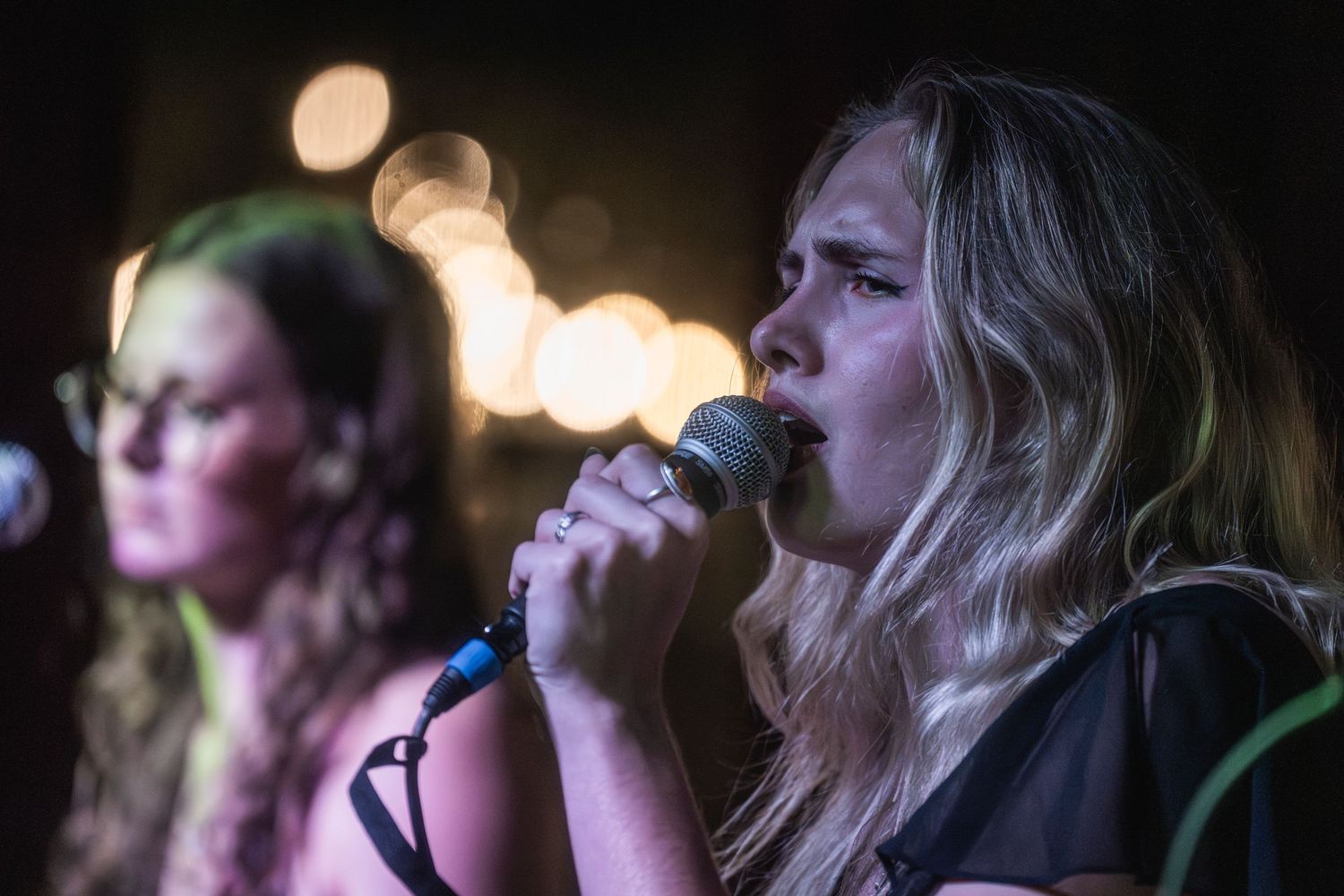 Concert audience members watch intently in dark lighting with bokeh effects visible in the background.