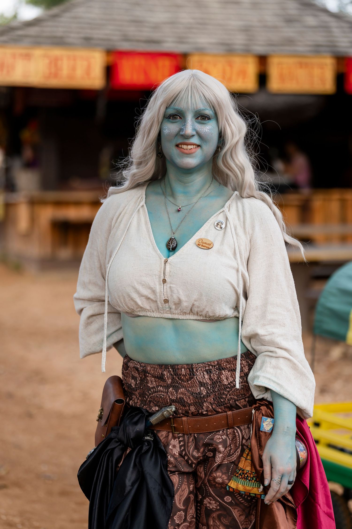A person in fantasy cosplay makeup with blue-tinted skin wearing a renaissance faire style costume and corset.