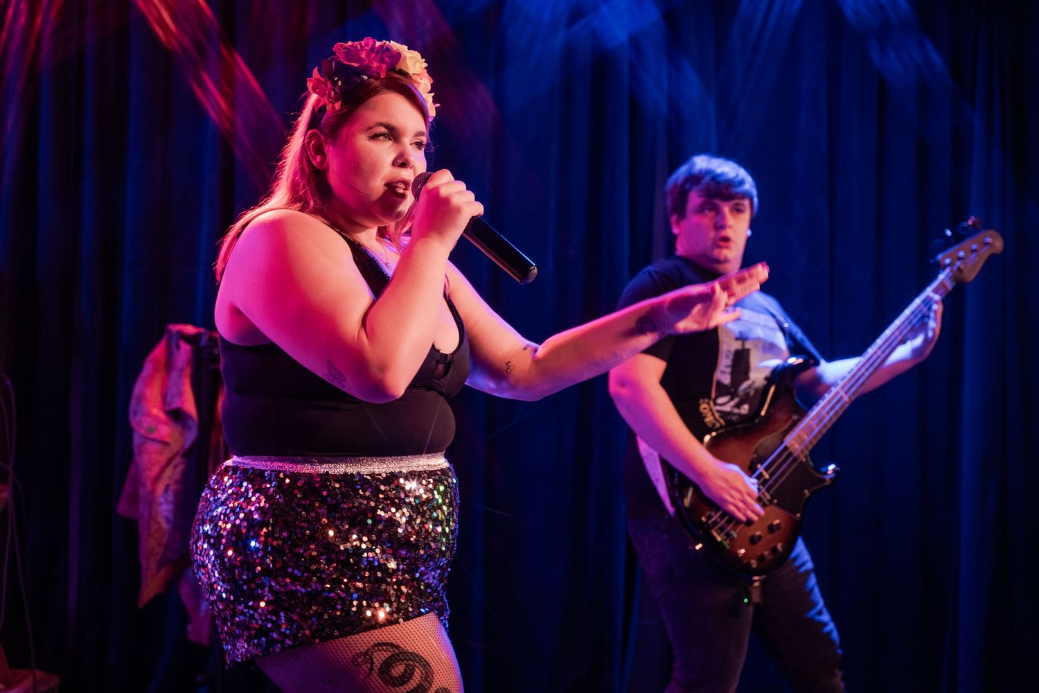 A performer in a sparkly dress sings on stage under dramatic blue and purple lighting during a live concert performance.