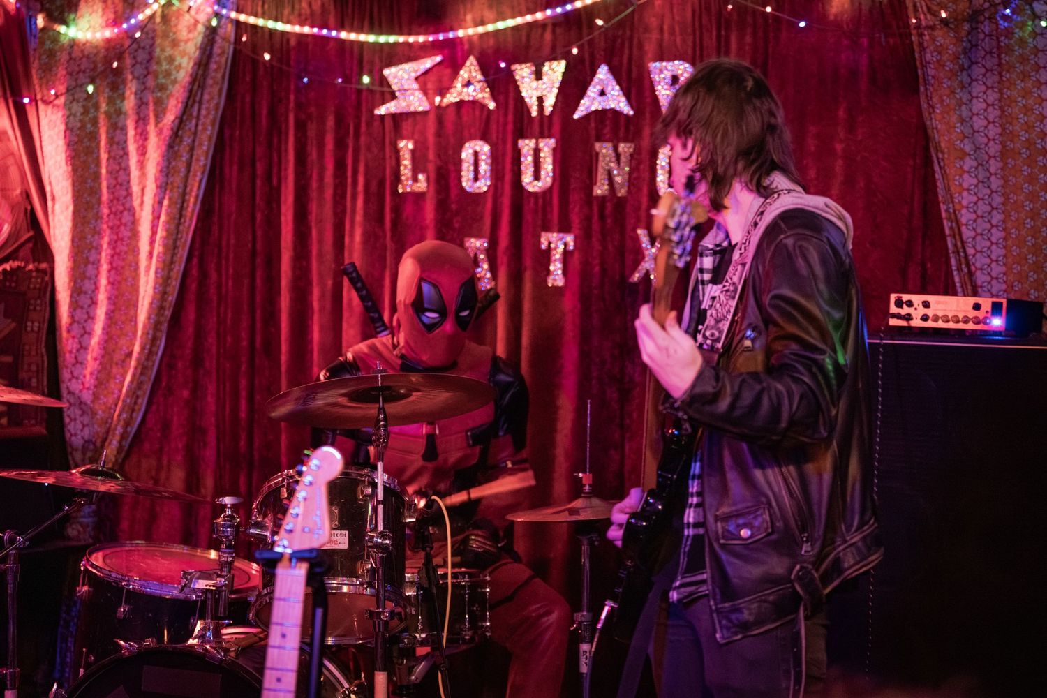 Musicians perform on stage at a dimly lit jazz lounge with red lighting and string lights creating an intimate atmosphere.