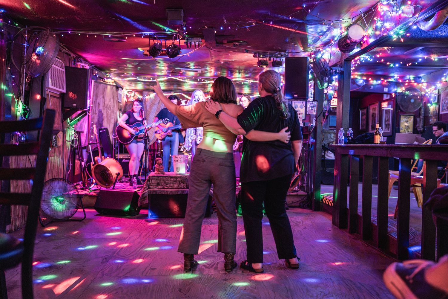 Nightclub interior with colorful pink and purple lighting illuminating a dance floor and seating area.