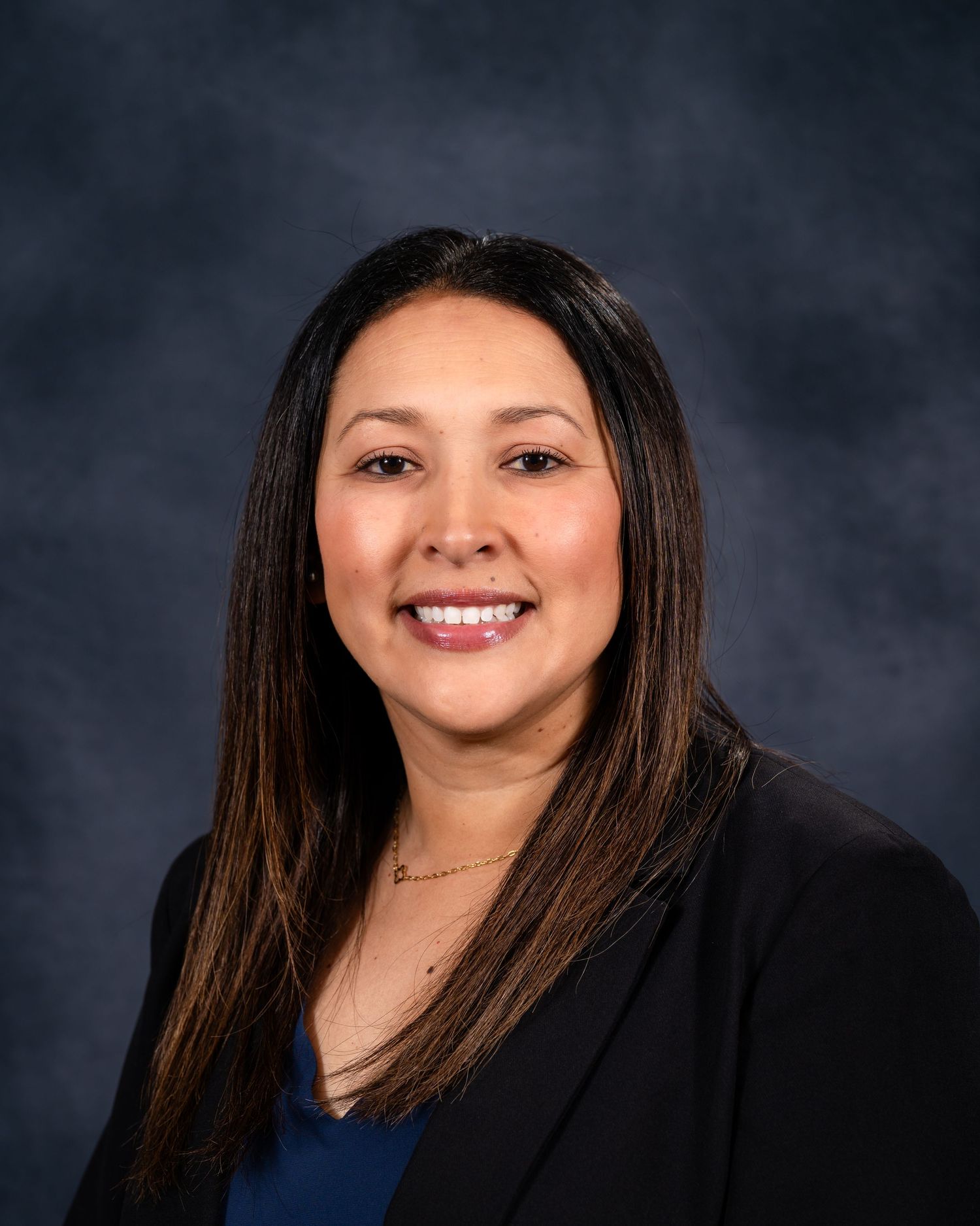 Professional headshot portrait against dark background wearing black blazer and smiling warmly.