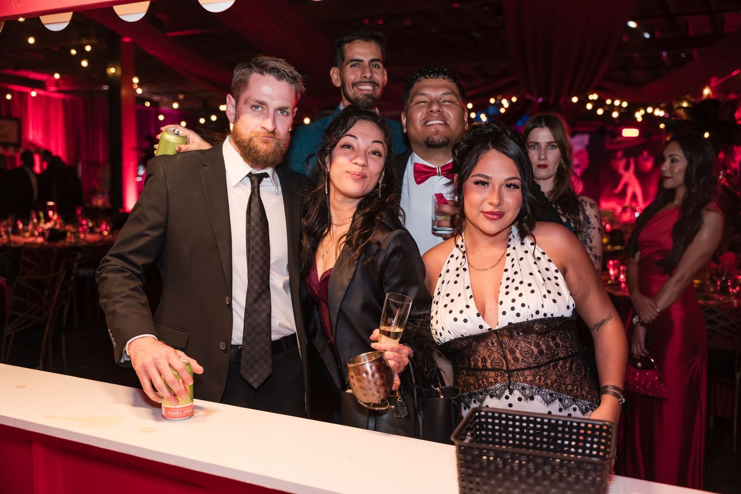 A group of people socialize at a dimly lit evening event with red ambient lighting.