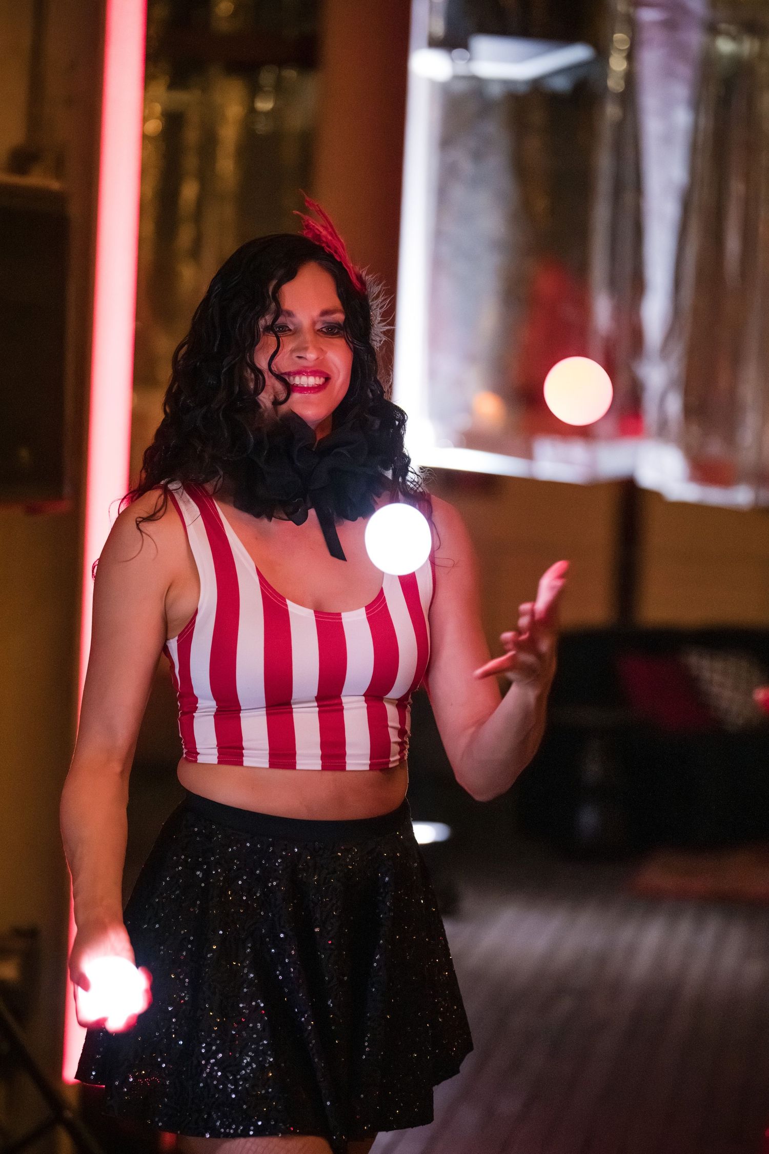 Woman in red and white striped top and sparkly black skirt poses joyfully in nighttime setting.