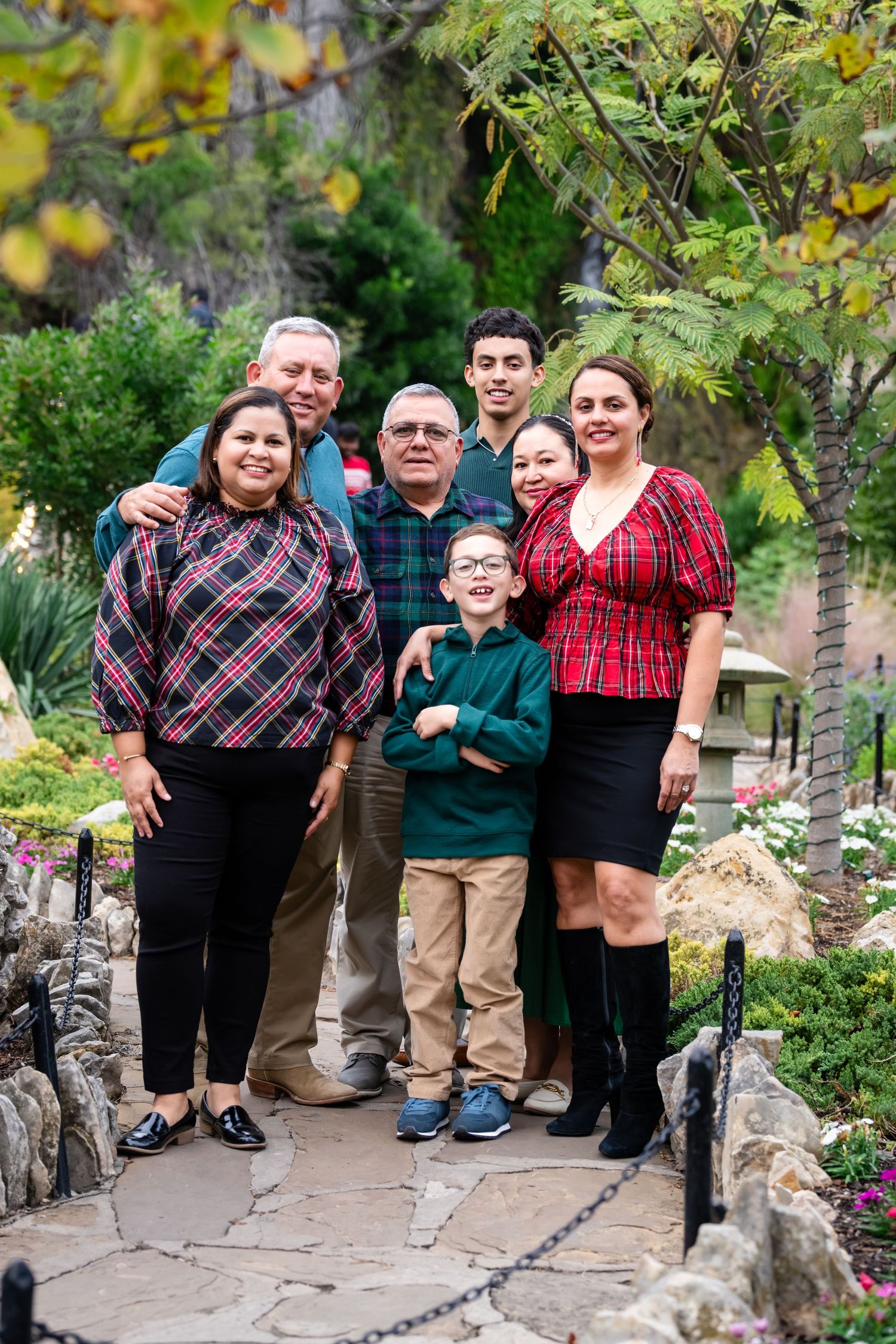 A family group poses together on a stone path in a garden setting with lush greenery and flowers in the background.