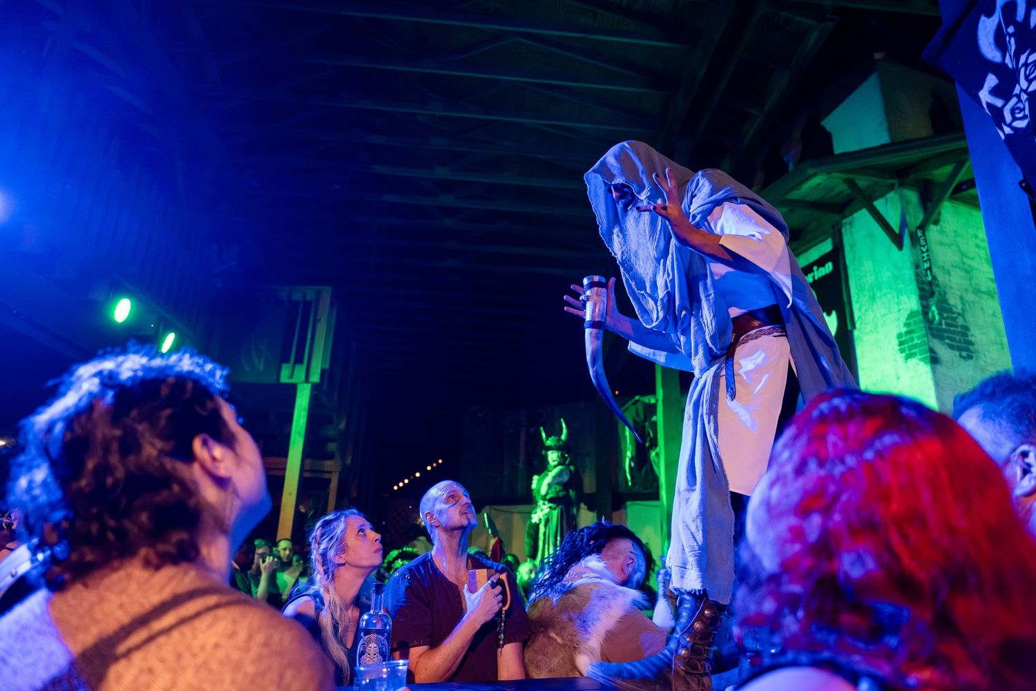 Concert performer on stage illuminated by blue and green lights as crowd watches from below during an energetic performance.