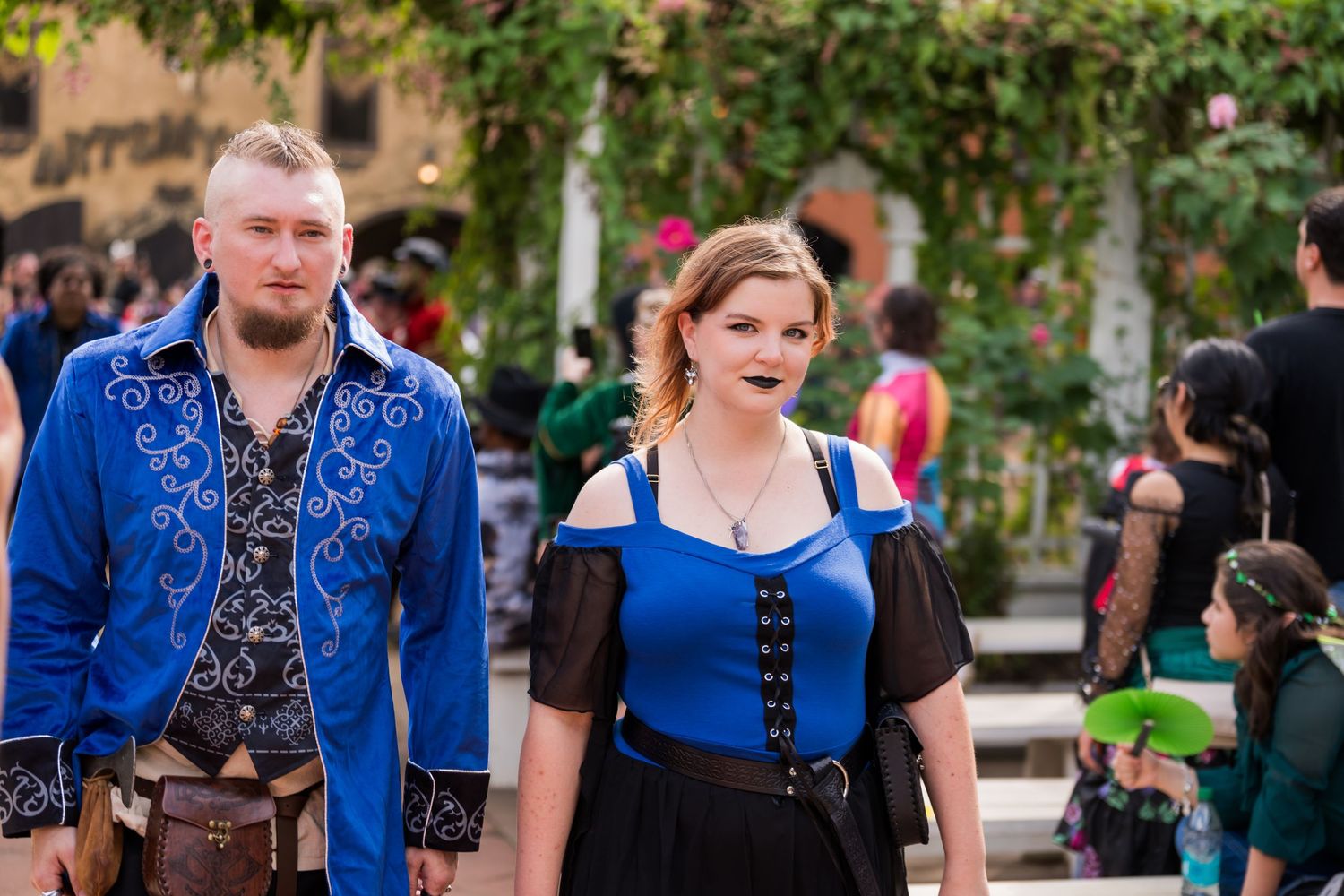 People in medieval costumes walk together at a renaissance fair wearing blue and black period clothing.