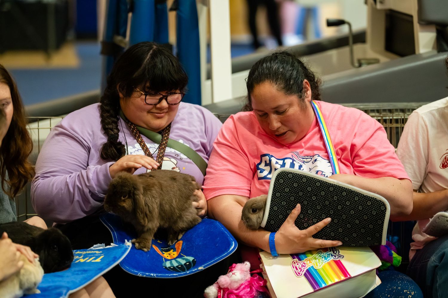 Two women interact with a small animal during an educational event, one holding a tablet device.