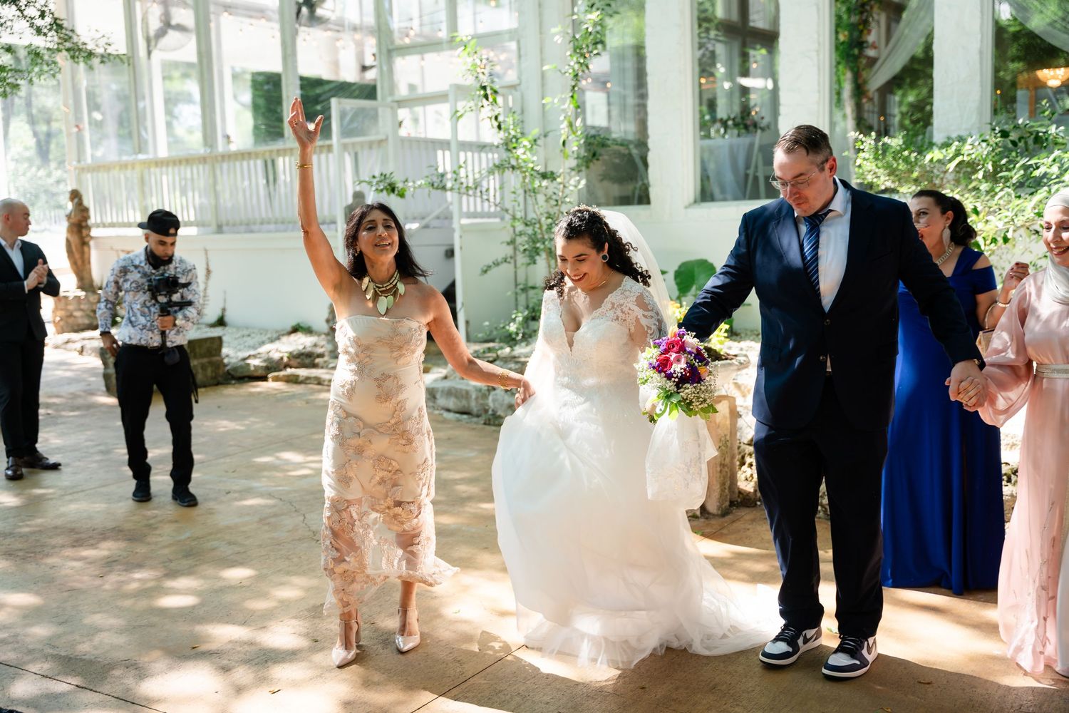 Bride in white gown celebrates with family at elegant indoor wedding venue, surrounded by guests in formal attire.