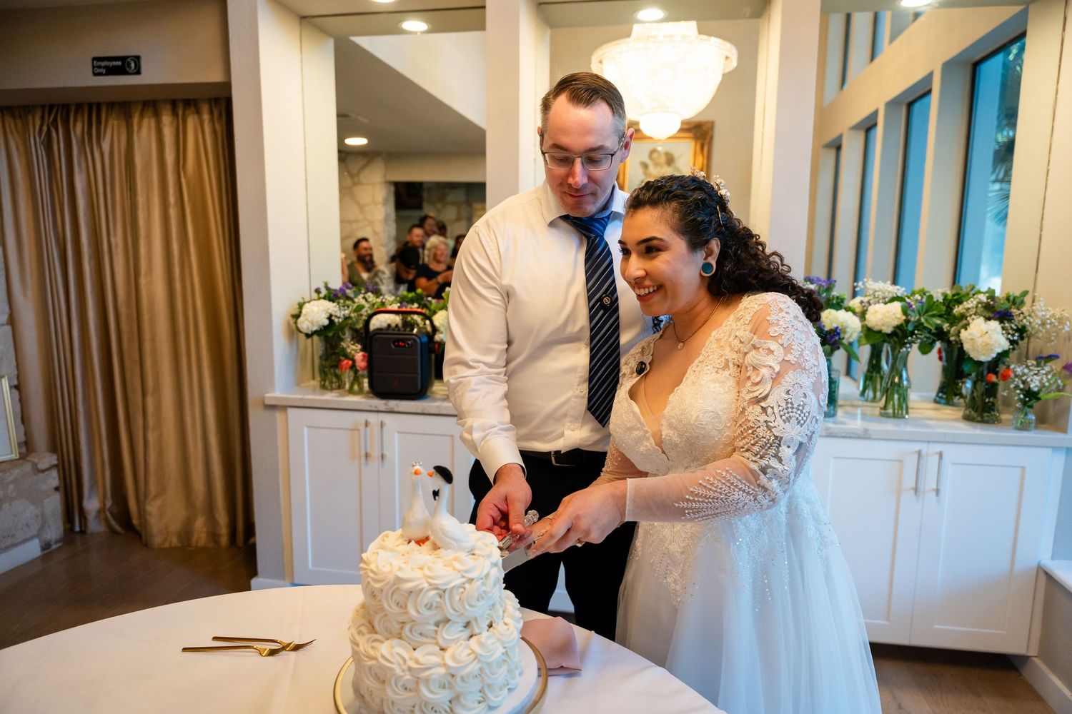 Bride and groom cutting their white wedding cake together at their elegant indoor wedding reception.