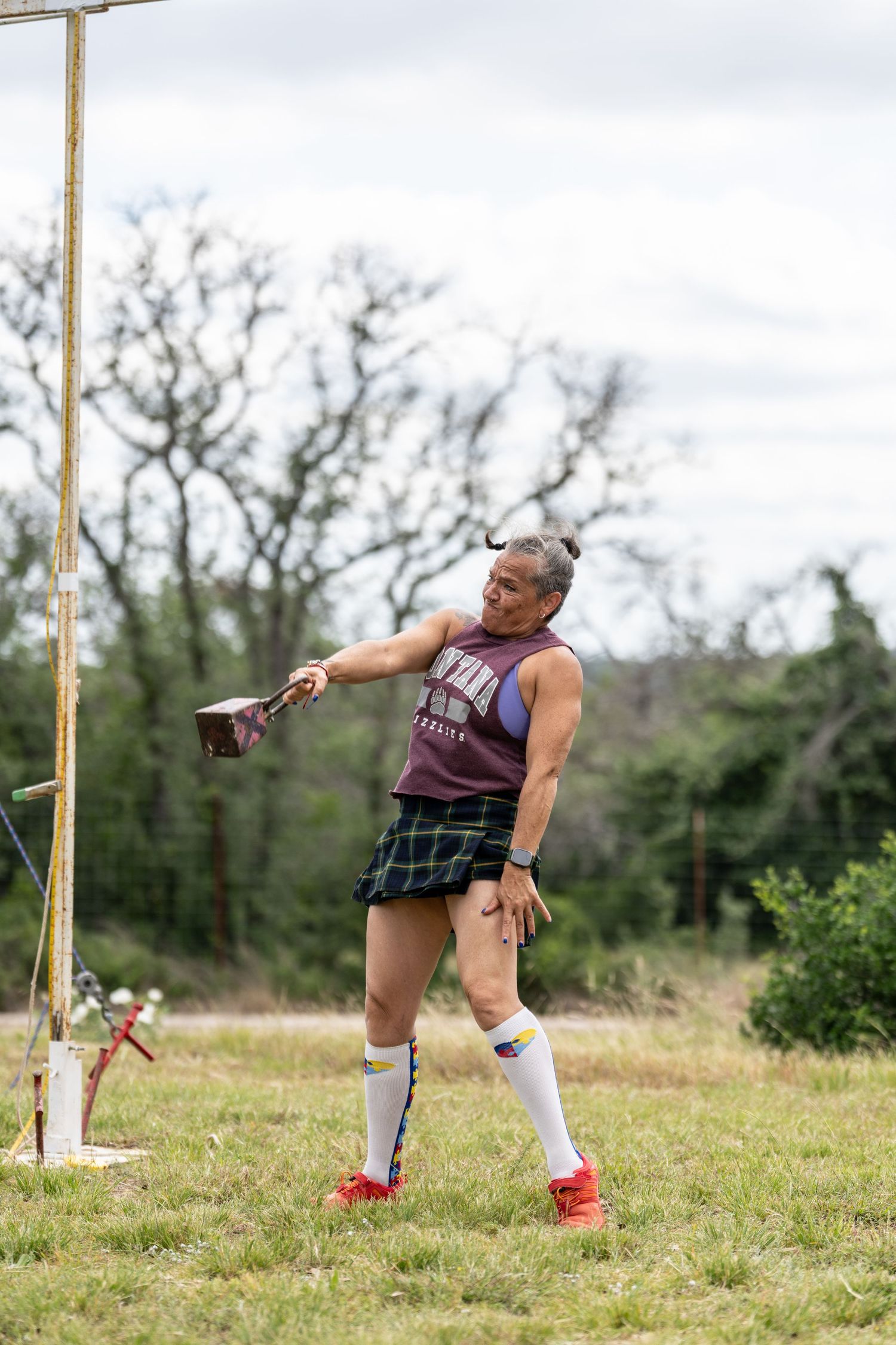 Athlete in tartan kilt and white socks competes in Highland Games hammer throw on grassy field.