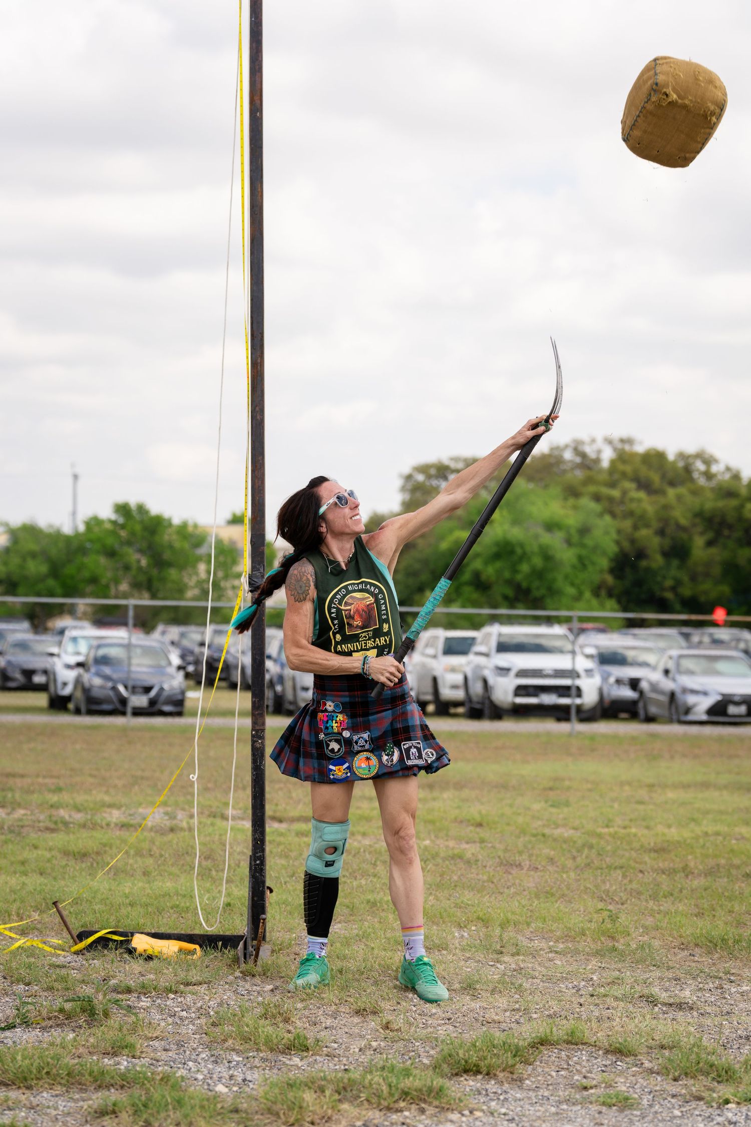 Athlete in tartan kilt tosses weighted ball at Highland Games competition outdoors.