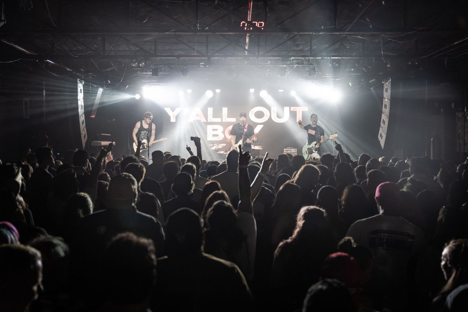 Fall Out Boy performing live on stage with dramatic lighting and a large crowd of fans at an indoor concert venue.