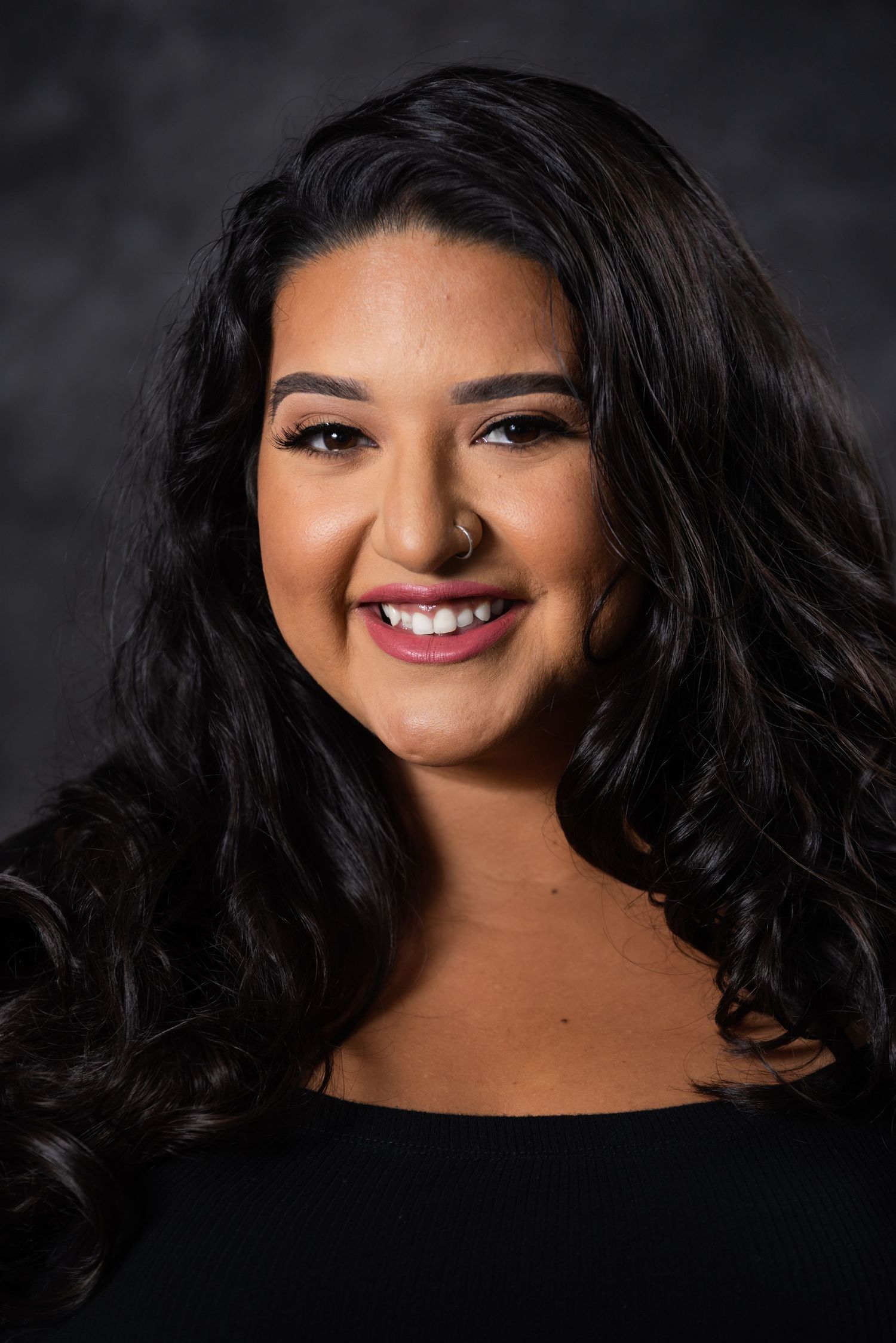 Professional headshot showing radiant expression and styled dark waves against charcoal background.