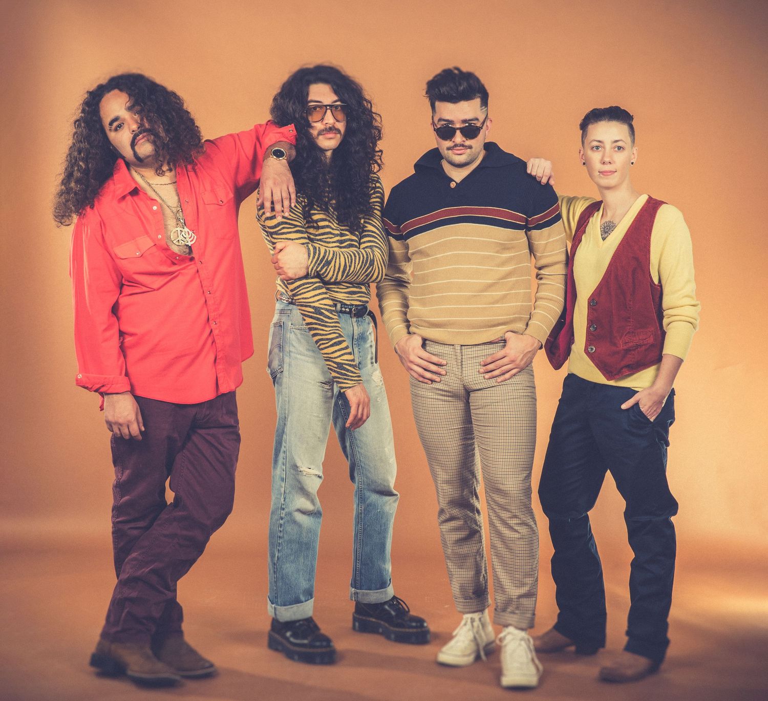 Four band members posing in casual attire against orange studio background.