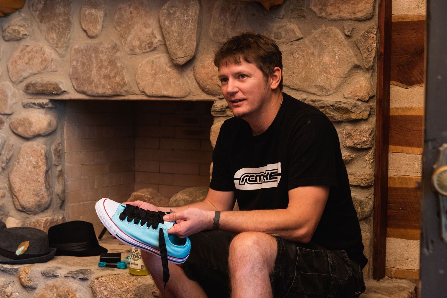 A person sits by a stone fireplace examining a light blue sneaker.