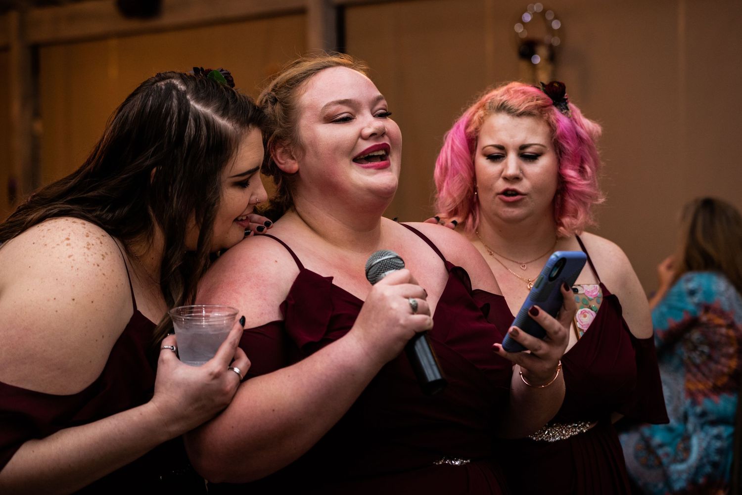 Bridesmaids in burgundy dresses check their phones during wedding reception celebrations.