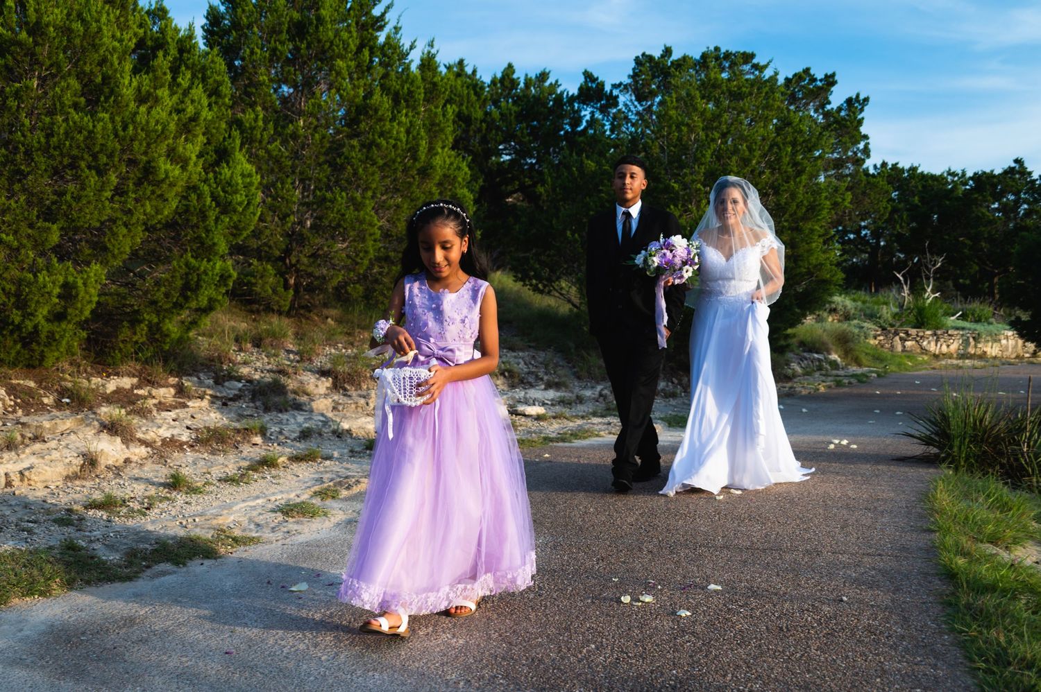 Wedding party poses on outdoor path with pine trees and scenic landscape in background.