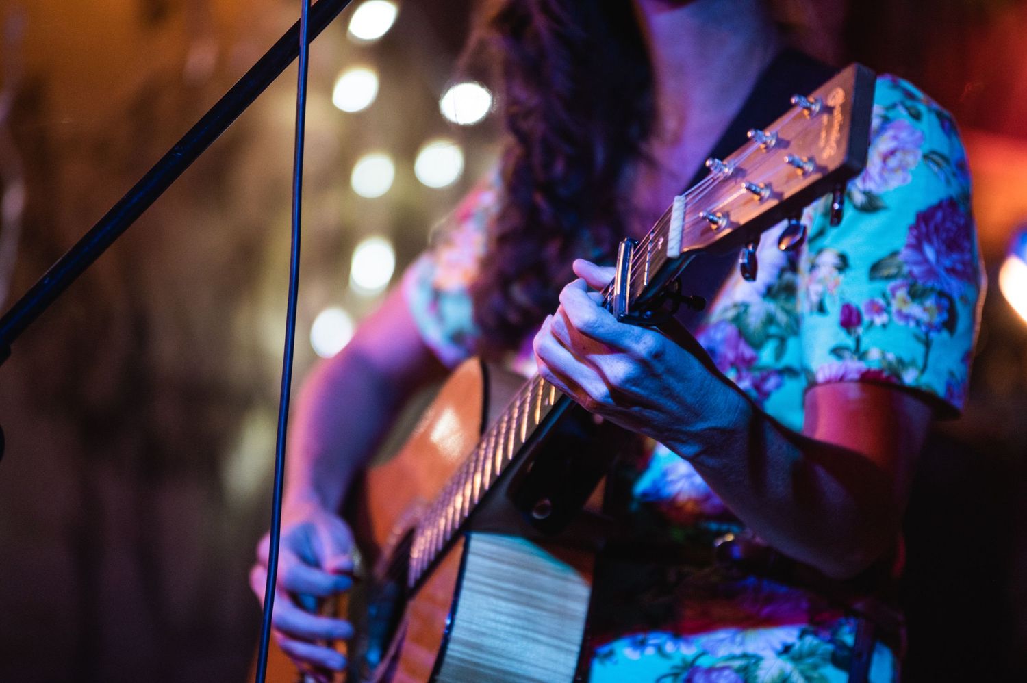 Close-up of hands playing acoustic guitar while wearing floral print dress.