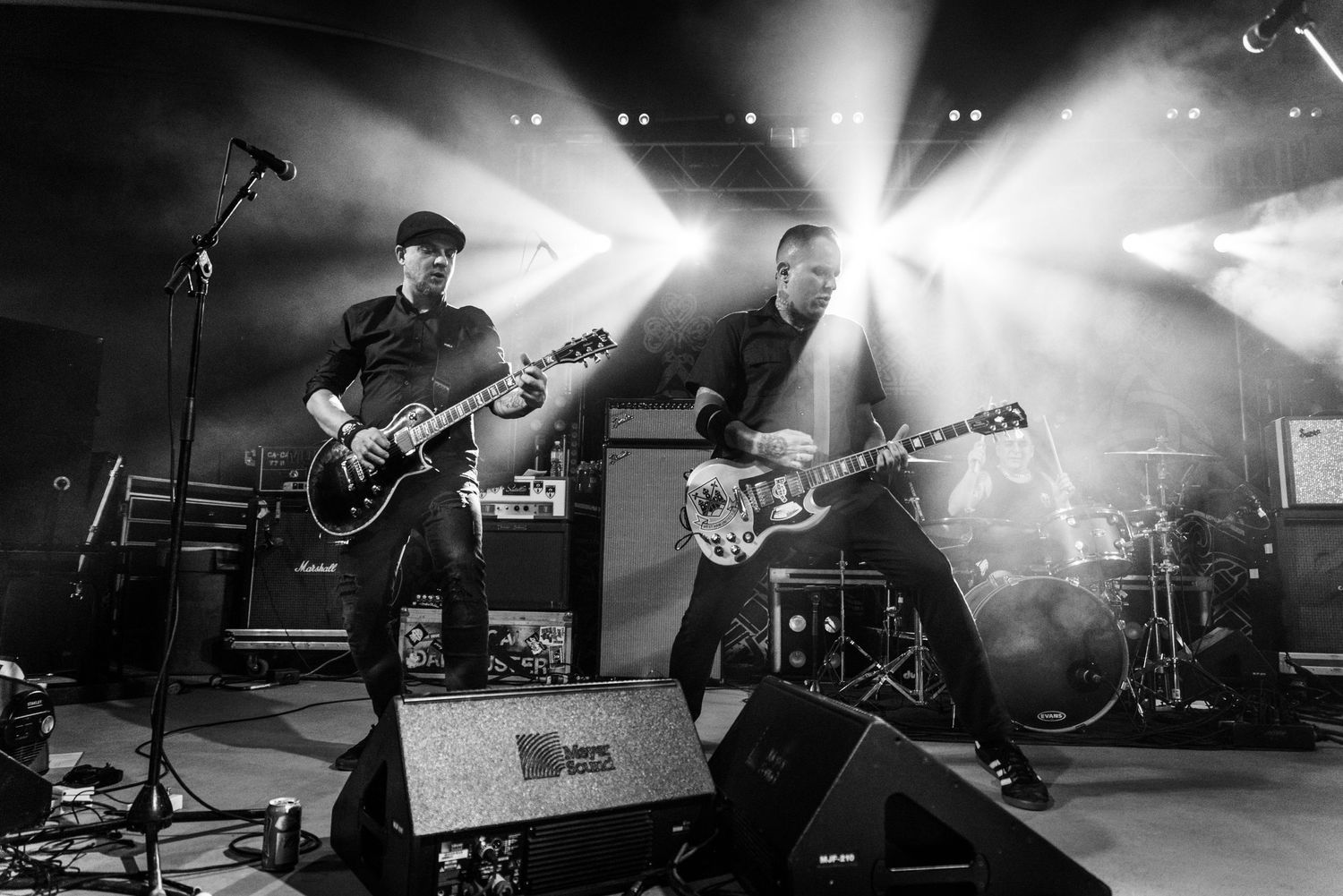 Rock band performs energetically on stage with guitarists silhouetted against dramatic backlighting and fog effects.