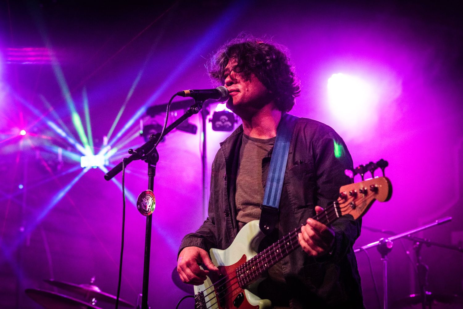 A musician performs with a bass guitar under vibrant purple stage lights.