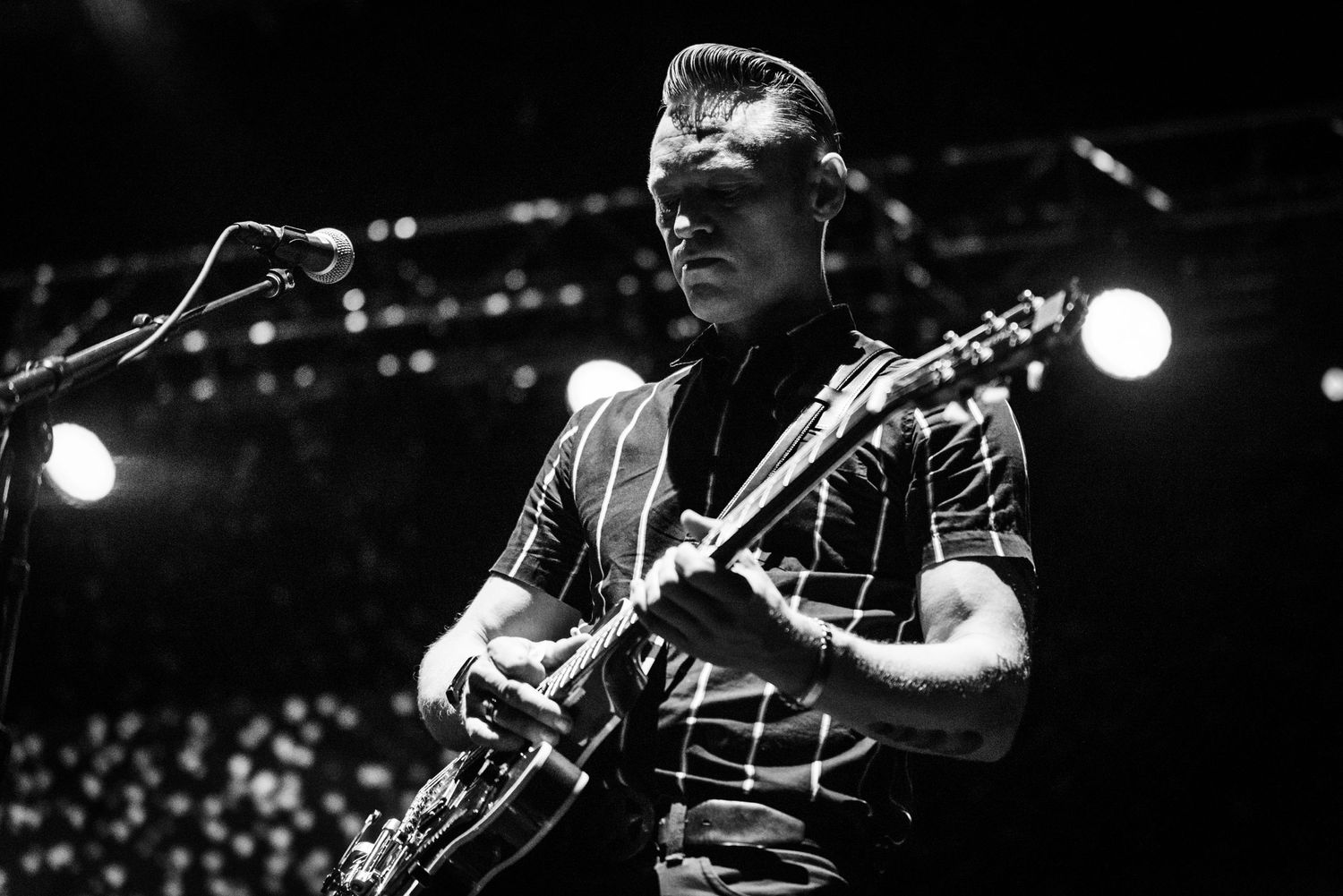 A performer plays guitar during a concert with dramatic stage lighting and microphone setup visible.