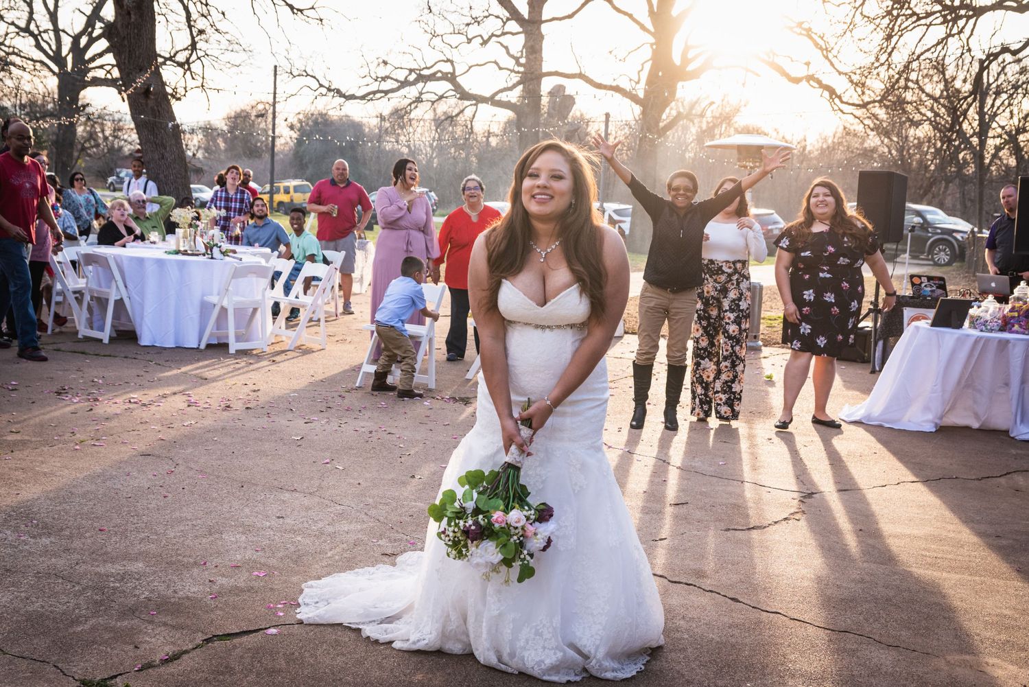 Bride in white gown poses with bouquet during golden hour at outdoor wedding reception.