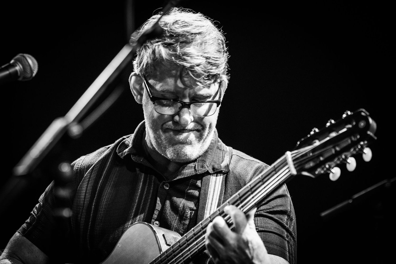 Black and white concert photo of musician performing with acoustic guitar against dark background.