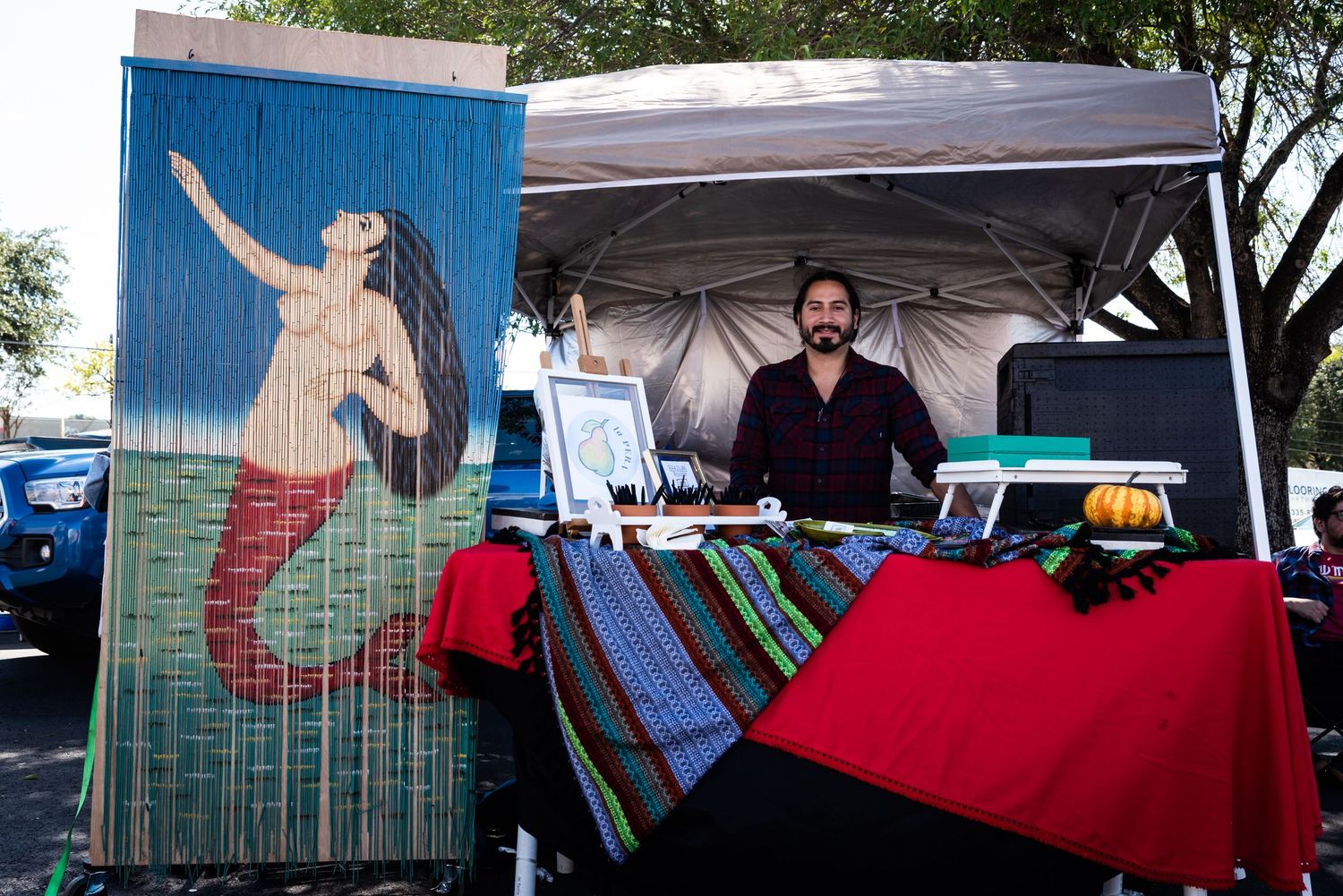 Vendor booth setup with artistic mural display and merchandise table.