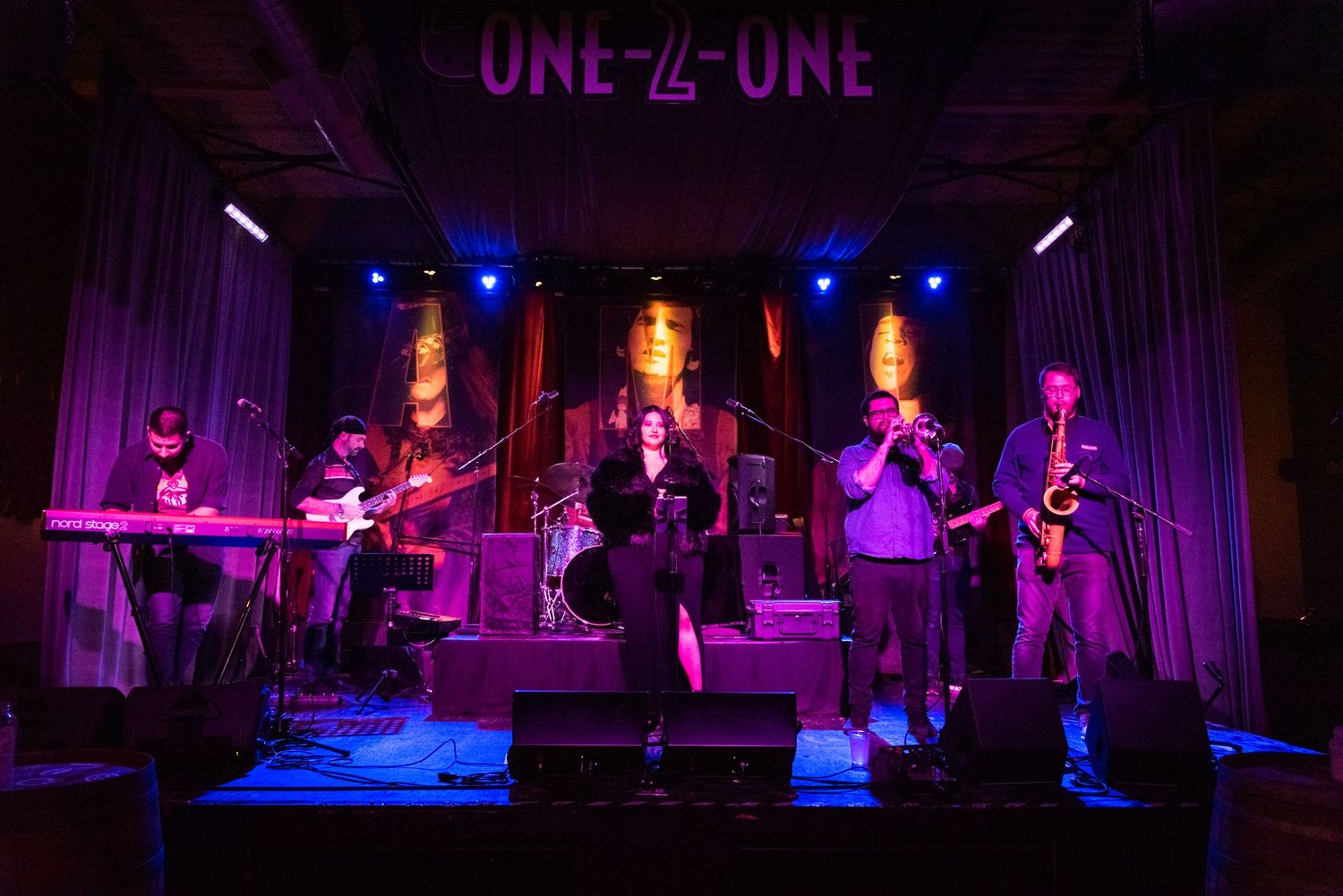Band performs on stage at One-2-One venue with colorful purple and blue lighting effects.