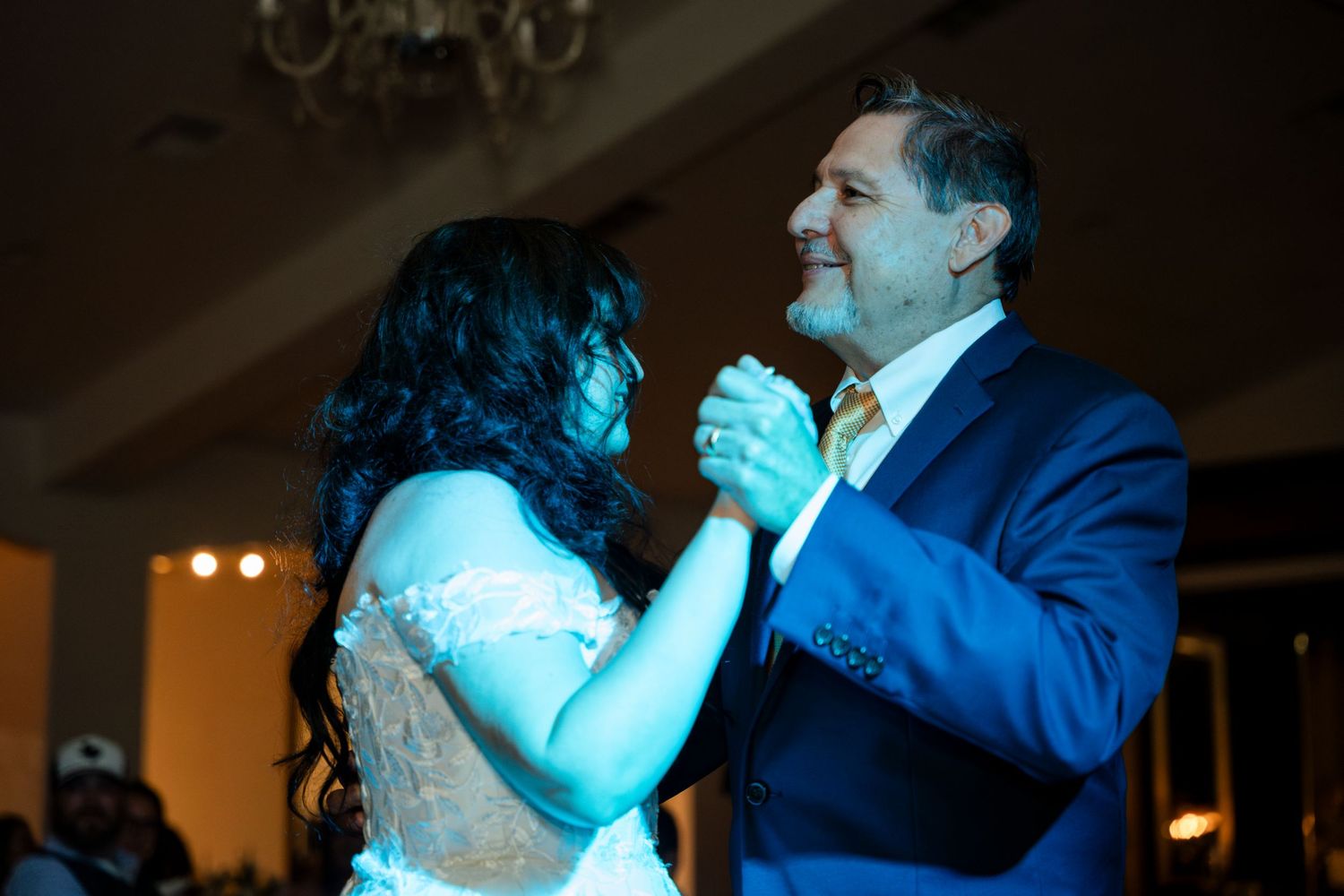 Couple in formal attire dancing at a wedding reception with blue lighting in the background.