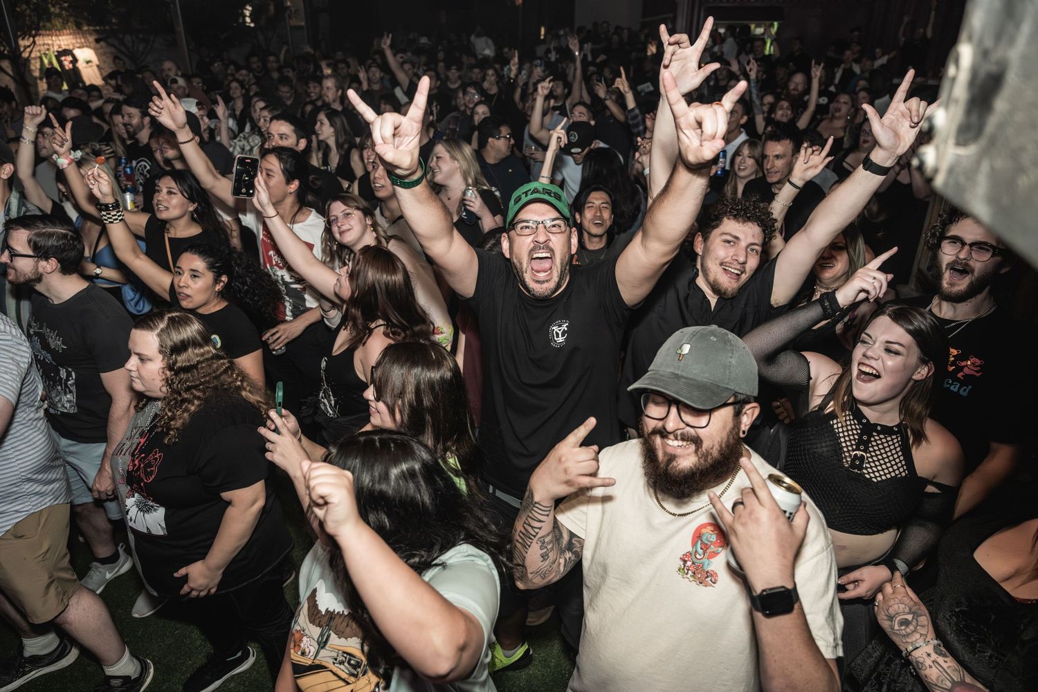 An enthusiastic crowd throws their hands up and makes rock gestures during a concert performance.