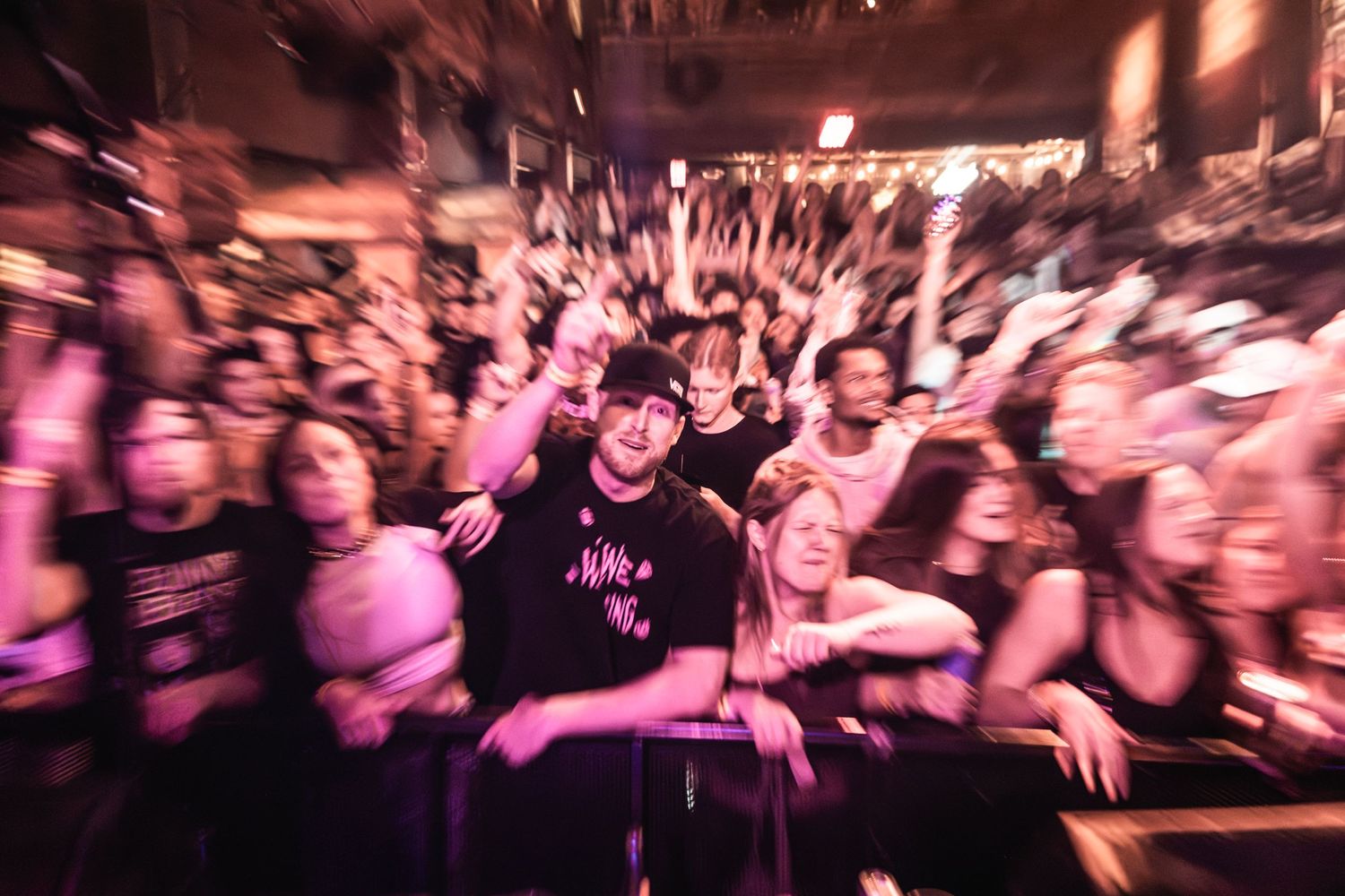 Blurred motion shot of concert crowd cheering with pink lighting effects.