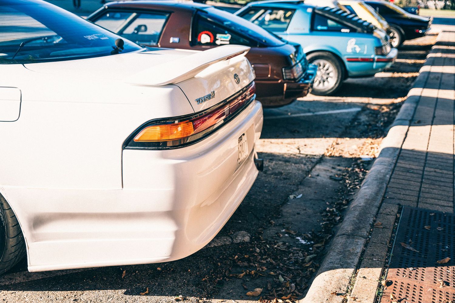 Close-up of white sports car rear ends in a car show lineup.