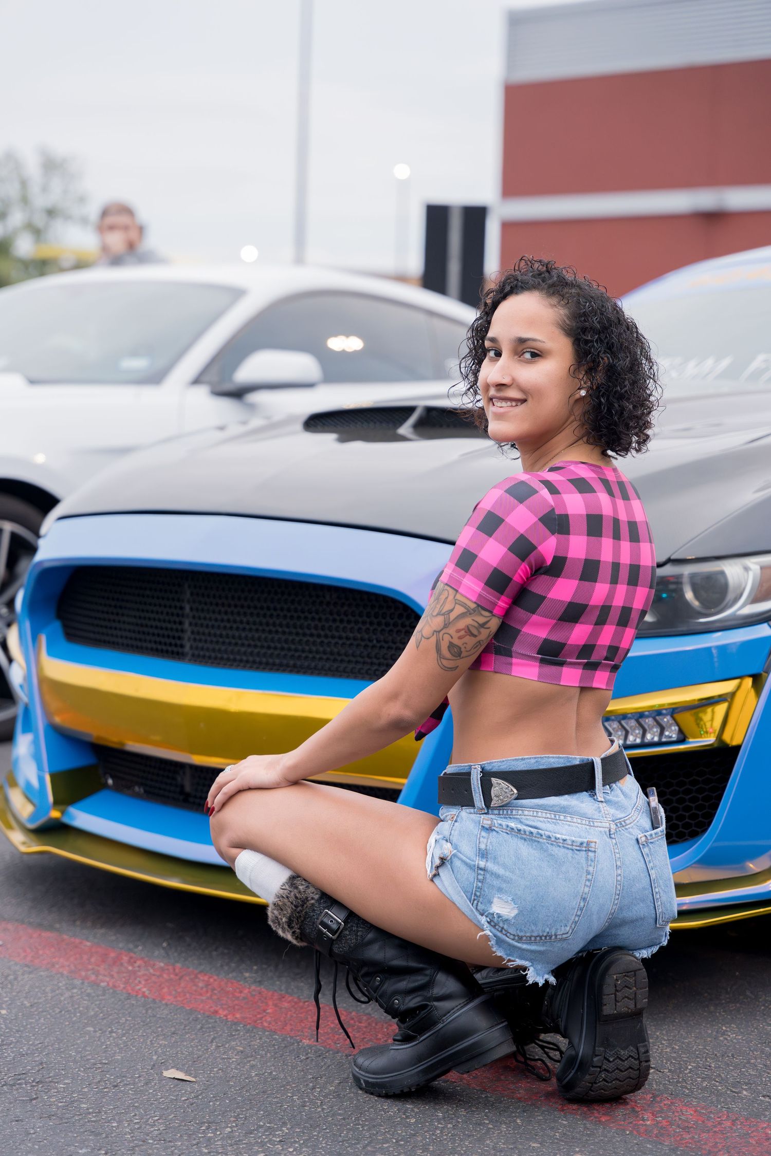 Pink plaid crop top and shorts outfit posed by customized blue sports car.