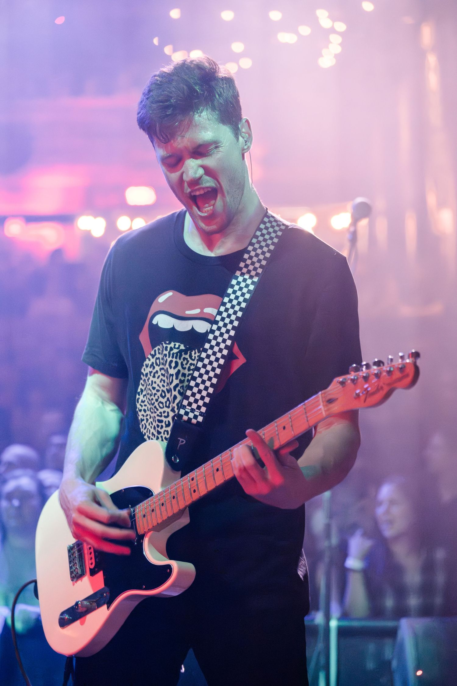 Guitarist plays electric guitar while performing under colorful stage lighting.