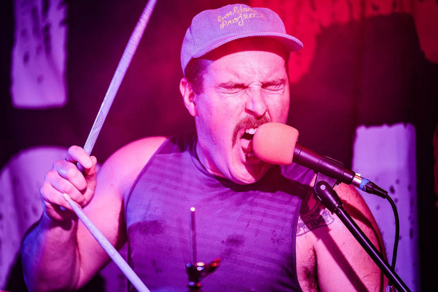 Performer singing passionately into microphone under intense red stage lighting.
