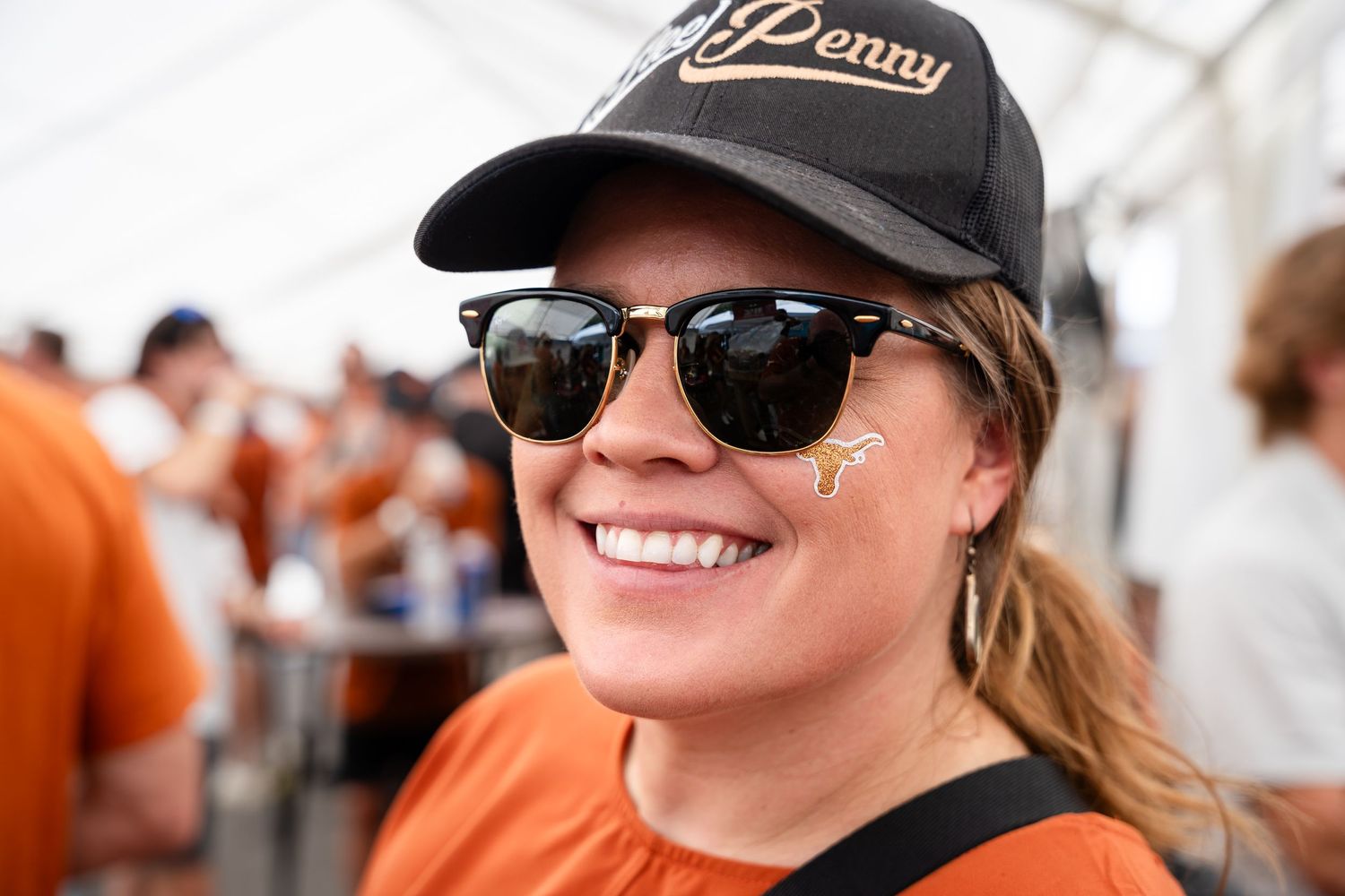 Festival attendee in a black cap and sunglasses smiles at a crowded outdoor event.