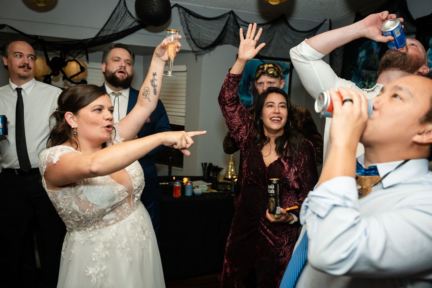 Wedding guests dancing and celebrating with drinks at an indoor party with dark decor.
