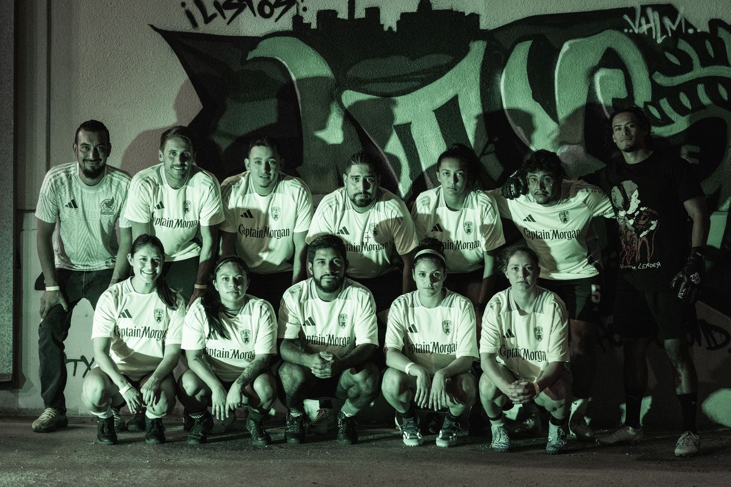 Team photo of athletes in white uniforms posing together against a graffiti wall.