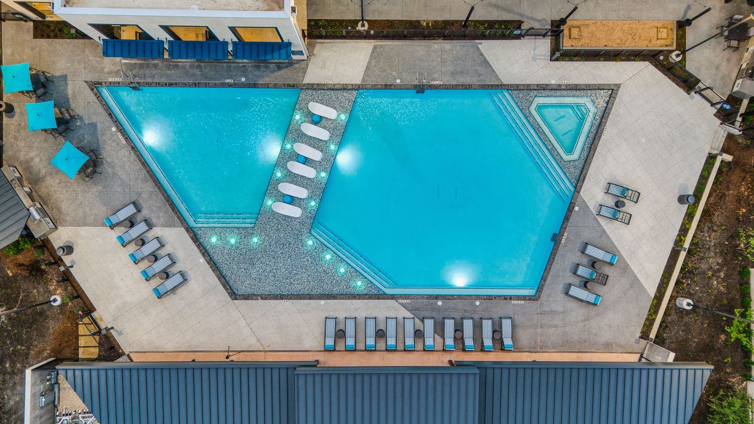 Bird's eye view of uniquely shaped swimming pool with symmetrical lounge chair arrangement.