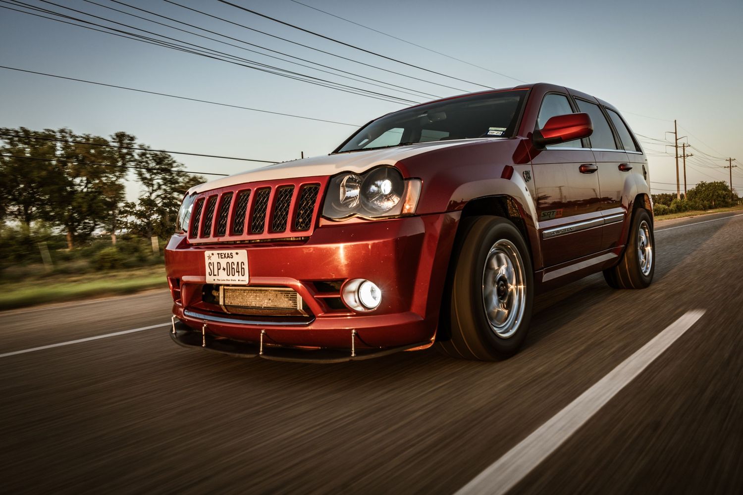 Modified maroon Jeep Grand Cherokee SRT8 cruising on street at sunset.