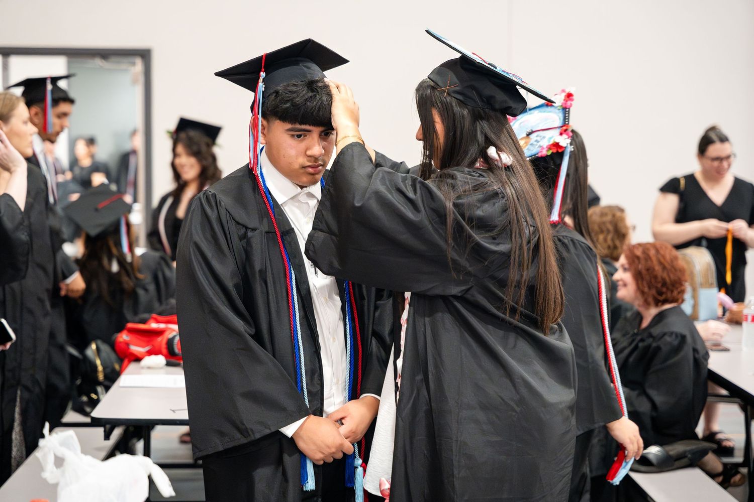 Graduates in traditional academic regalia adjusting each others caps and gowns.
