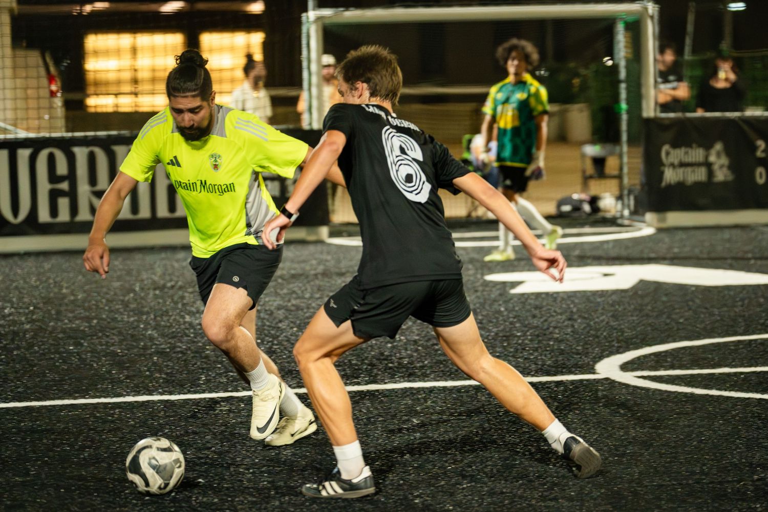 Two players battle for ball control during a competitive indoor soccer match.