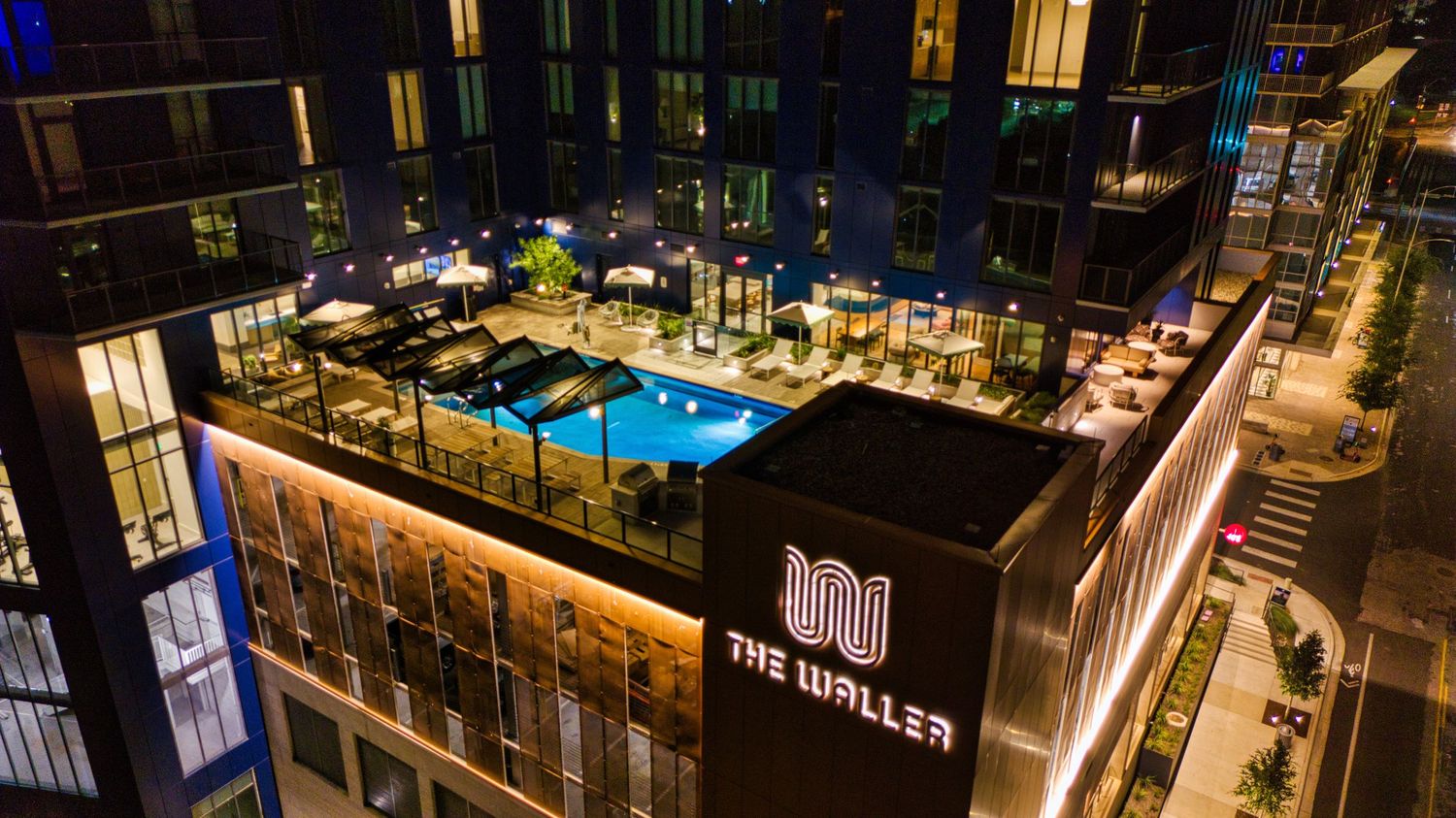 Illuminated rooftop pool and lounge area of The Waller hotel at night with modern architectural lighting.