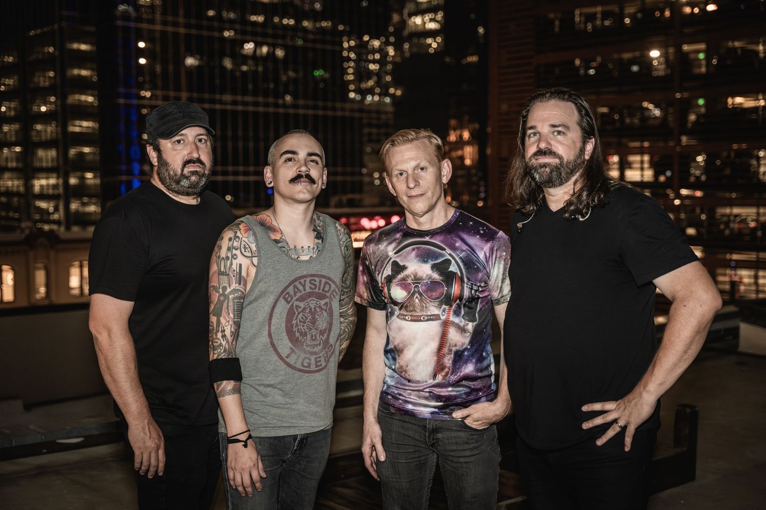 Rock band members pose on a rooftop at night with city skyline backdrop.