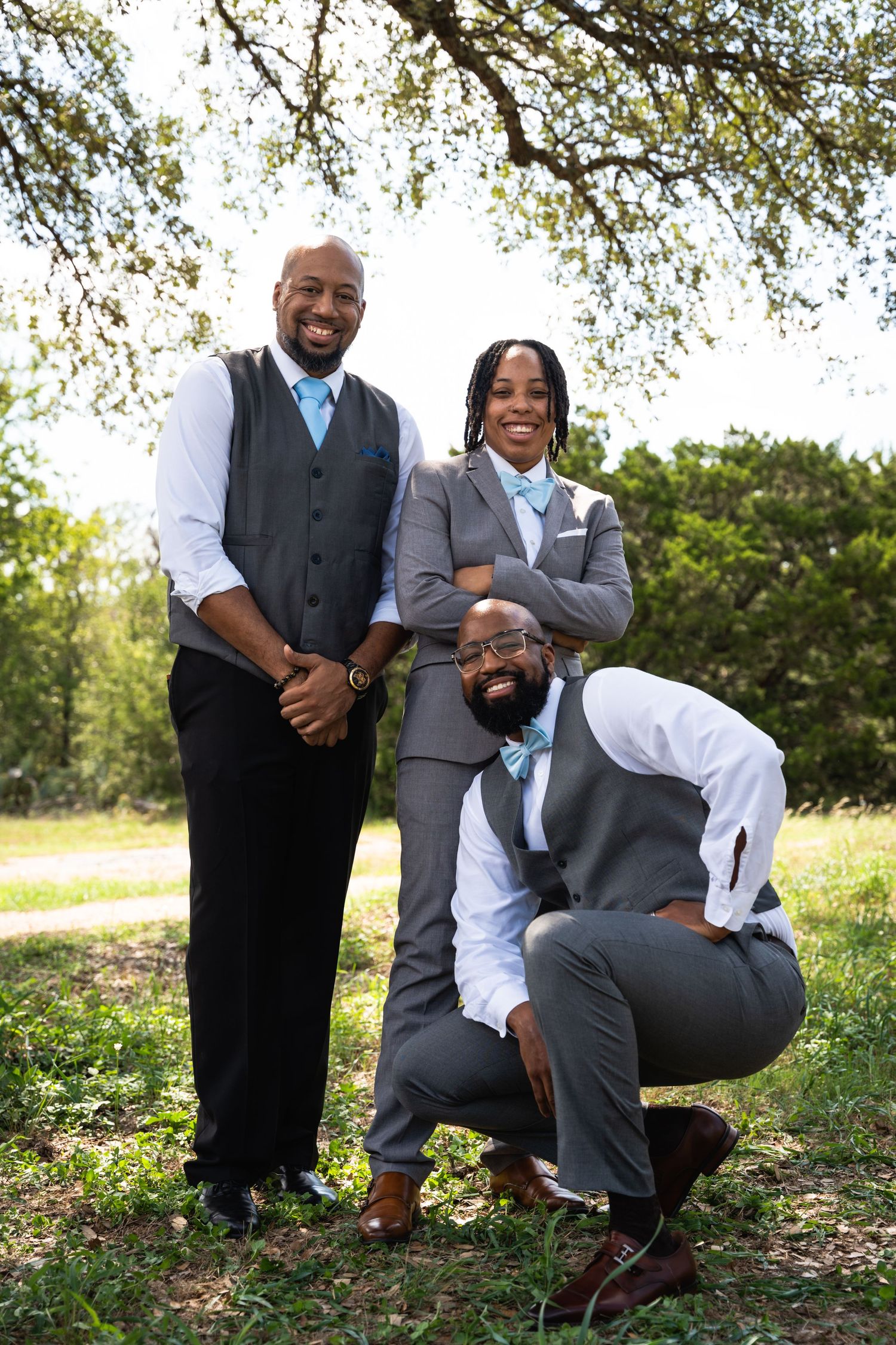 Three people in formal business attire pose playfully outdoors.