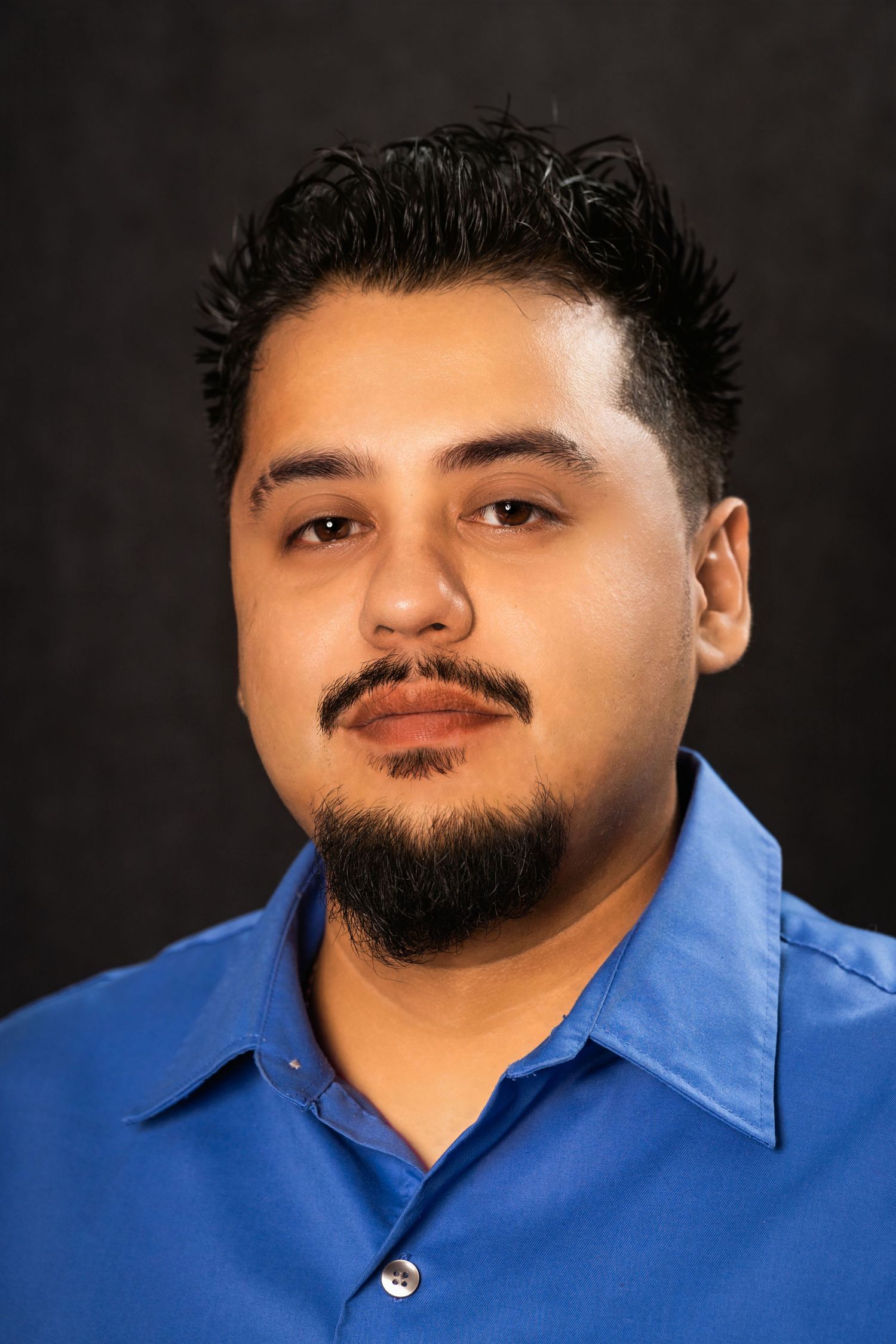 Professional headshot of a man wearing a blue collared shirt against a dark background.