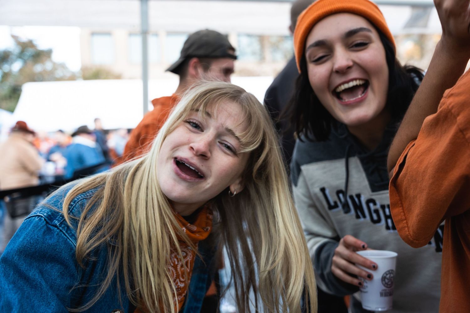 College friends laughing and celebrating together at an outdoor university event wearing orange and blue team colors.