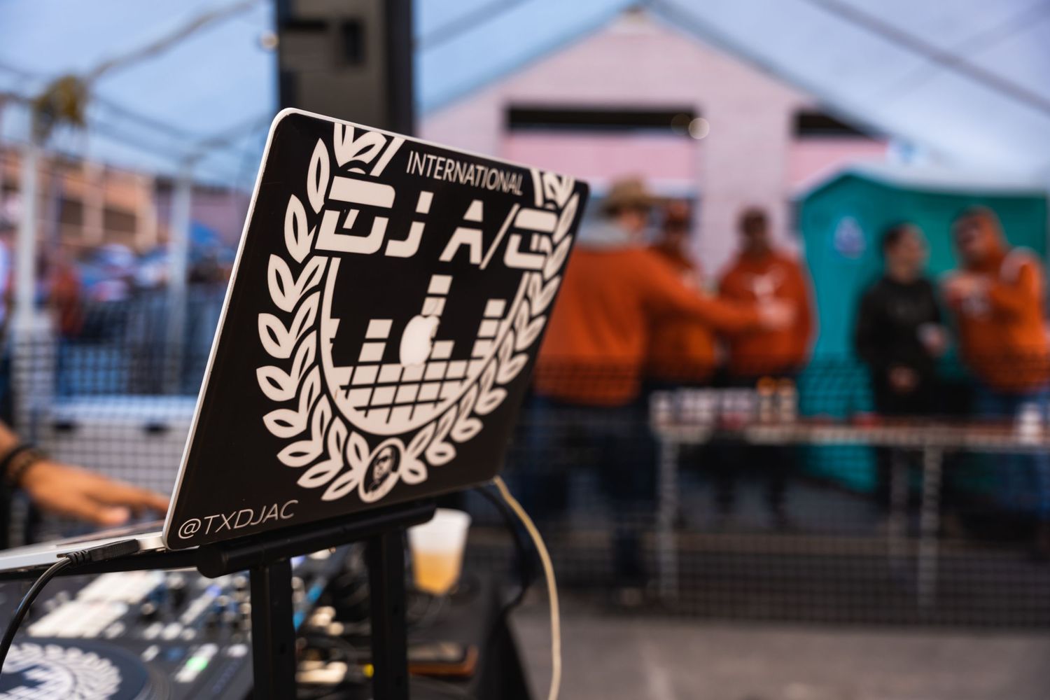 Close-up of a DJ equipment logo with laurel wreath design against blurred background.
